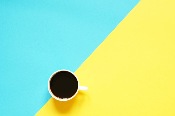 Taza plana de café negro sobre fondo amarillo y azul. Concepto alimentario minimalista
. - Foto, Imagen