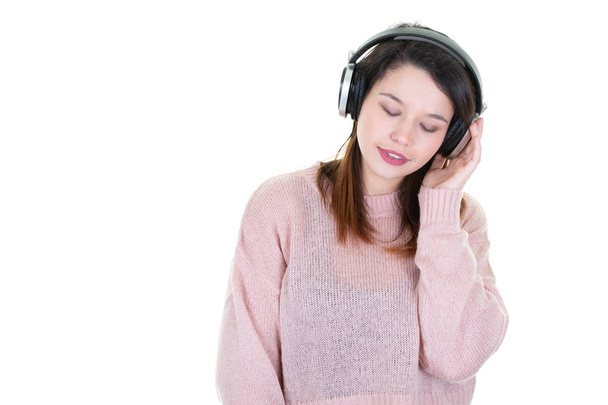 Hnědá černovlasá dívka se sluchátky naslouchající hudbě s zavřenýma očima na bílém pozadí s stranou kopírovací prostory - Fotografie, Obrázek