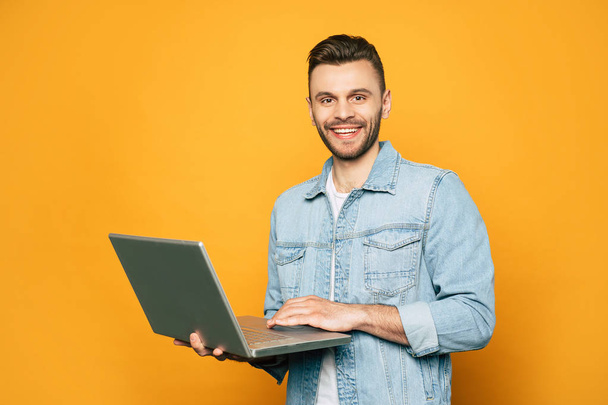 Modern young student or business man is working with laptop in hands on yellow background - Photo, image