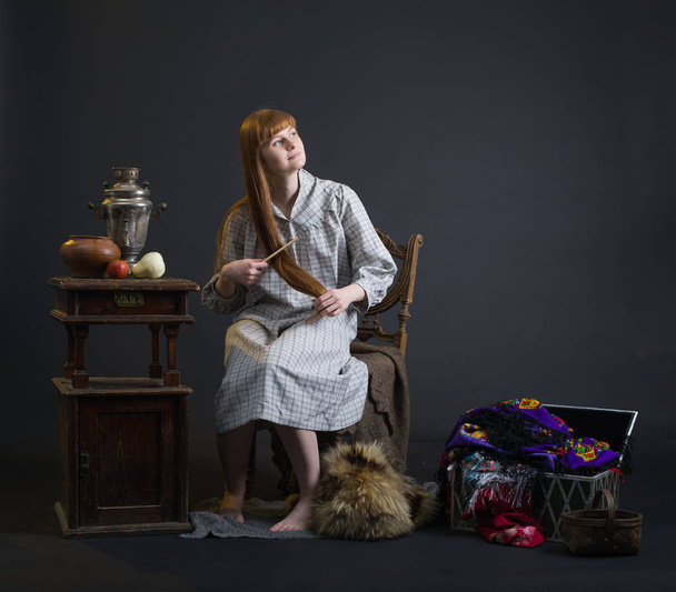 Молода жінка слов'янської зовнішності гребінця її червоне волосся в оточенні ретро-речей. - Фото, зображення