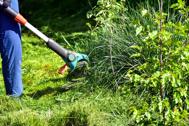 die einfachen Momente des Lebens, die gewöhnliche Arbeit im Garten - Mann trimmt Gras mit Hochleistungstrimmer im Garten, geeignet zum Trimmen langer Rasenkanten und größerer schwer zugänglicher Flächen - Foto, Bild