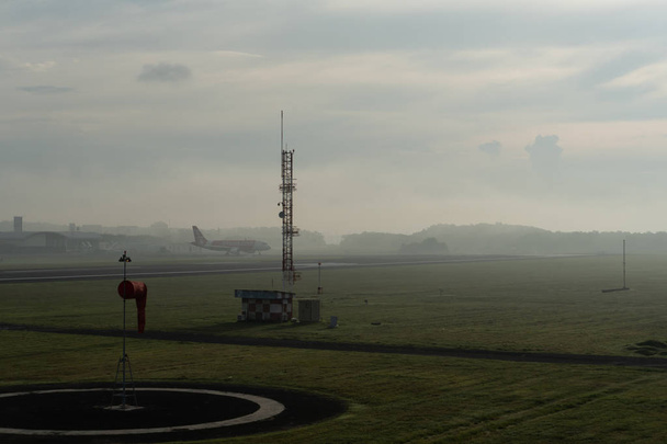 badung / bali-april 14 2019: eine Landschaft des meteorologischen Gartens am ngurah rai Flughafen bali am Morgen, wenn der Himmel voller grauer Cirruswolken ist und ein Flugzeug landet - Foto, Bild