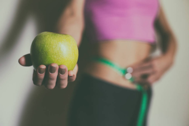 Fit woman measuring her tin waist  with a tape measure and showing apple.Focus on apple.Weight loss concept. - Zdjęcie, obraz