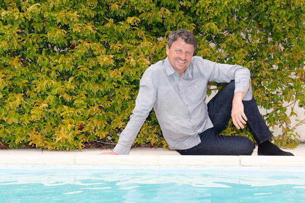 bonito homem sentado chão jardim perto de piscina deck
 - Foto, Imagem