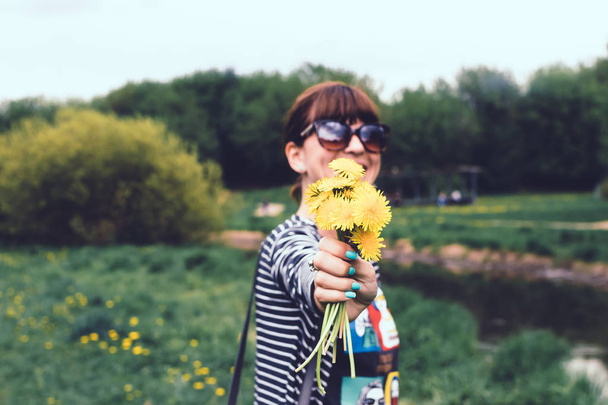 Jonge mooie vrouw met gele paardebloemen in het zonnige zomer Park. - Foto, afbeelding