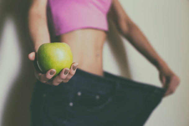 Woman in large jeans holding apple.Focus on apple.Weight loss concept. - Valokuva, kuva