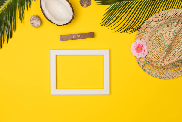 Stylish summer composition with photo frame, green leaves, hat and coconut on a yellow background. Artwork mockup with copy space - Foto, afbeelding