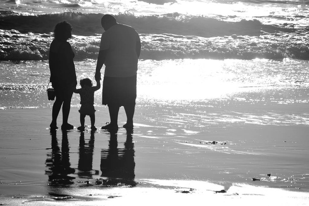 Молодая семья на отдыхе на пляже. Дети первые шаги со своей семьей на пляже Санта-Моника. черный и белый
. - Фото, изображение