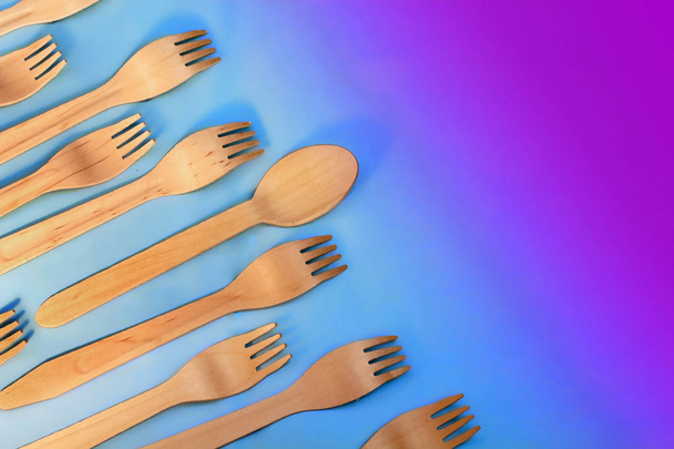 Disposable ecological wooden bamboo fork and spoon pattern on a blue background. Environment friendly flat lay with free copy space for text. Selective background with purpule toning - Photo, Image