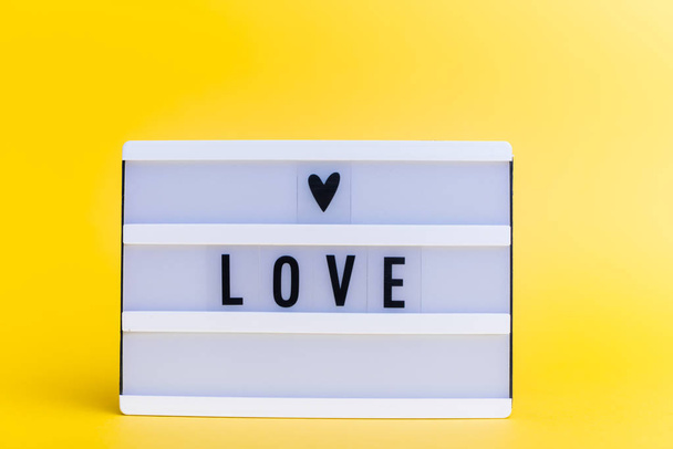 Φωτογραφία ενός ελαφρού κουτιού με κείμενο, Love, σε απομονωμένο κίτρινο φόντο - Φωτογραφία, εικόνα