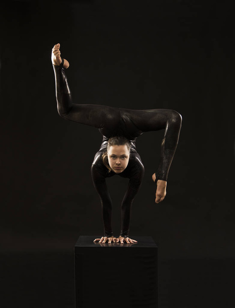 A charming girl gymnast, in a black suit, engaged in acrobatics in the light of the contra. - Фото, зображення