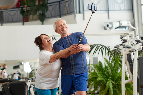 Happy couple of seniors using monopod at gym. - Fotoğraf, Görsel
