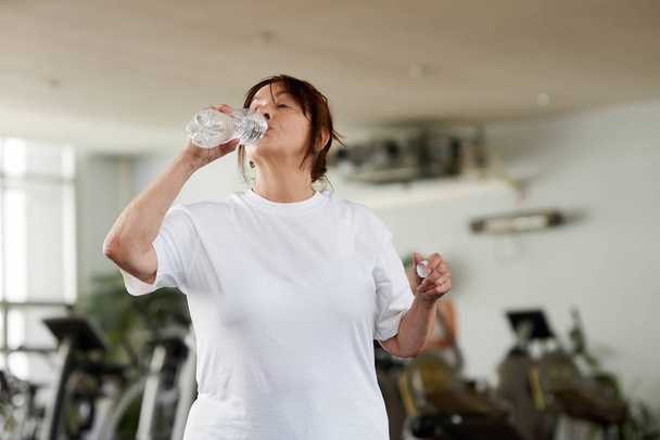 Senior woman drinking water after fitness training. - Foto, Imagem