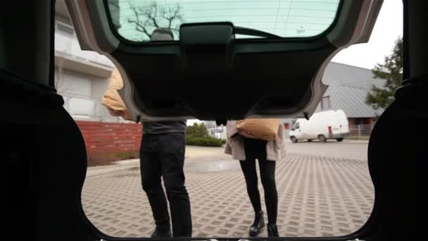 Νεαρό ζευγάρι συσκευασίας τσάντες ψώνια με φρέσκο φαγητό στο πορτ-μπαγκάζ του αυτοκινήτου, θέα από το εσωτερικό του οχήματος - Πλάνα, βίντεο