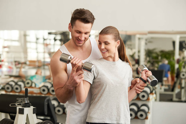 Personal trainer helping a young woman lift weights - Foto, immagini