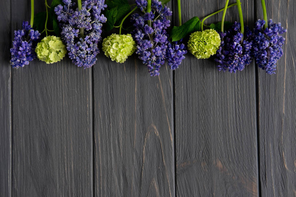 Hermosas flores de color púrpura y verde sobre un fondo de madera gris con espacio para la inscripción de saludo. Marco para banner de saludo, tarjeta de felicitación. Piso tendido, vista superior
. - Foto, imagen