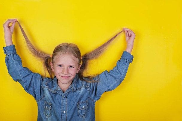 Смеющаяся маленькая девочка, стоящая на желтом фоне и держащая хвостики
 - Фото, изображение