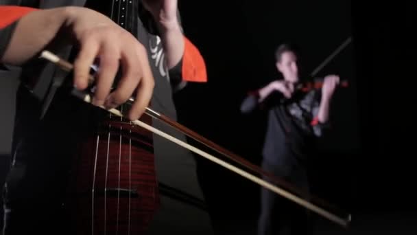 dúo de jóvenes tocando violonchelo eléctrico y violín eléctrico sobre un fondo negro, aislado
 - Metraje, vídeo