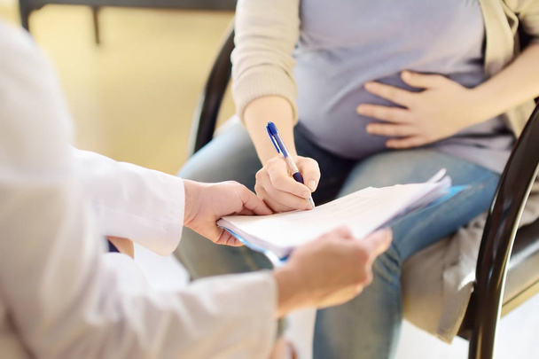 Pregnant woman sign the contract or permit during accepts of gynecologist doctor. Medical insurance childbearing. Family doctor for gestation. Maternity leave. - Valokuva, kuva