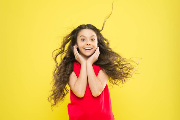 Věci, které děláš, aby sis zničil vlasy. Dívka rozkošné dítě dlouhé vlnité vlasy žluté pozadí. Vítr může také poškodit vlasy. Silné vytrvalé větry mohou vytvářet spletence a chňapnutí ve vlnitých a kudrnatých dlouhých vlasech - Fotografie, Obrázek