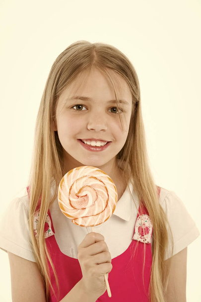 Girl smile with lollipop isolated on white. Small child smiling with candy on stick. Happy kid with swirl caramel. Food and dessert. Enjoying sweet lollipop. Diet and dieting - Valokuva, kuva
