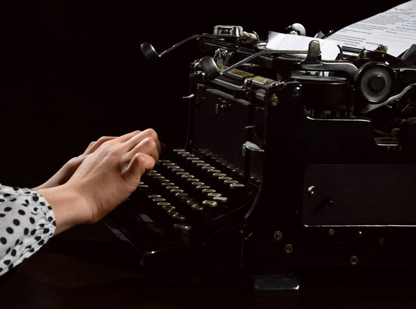 Κορίτσι χέρια δακτυλογράφηση γράμμα στην παλιά μηχανή γραφομηχανή στο μαύρο - Φωτογραφία, εικόνα