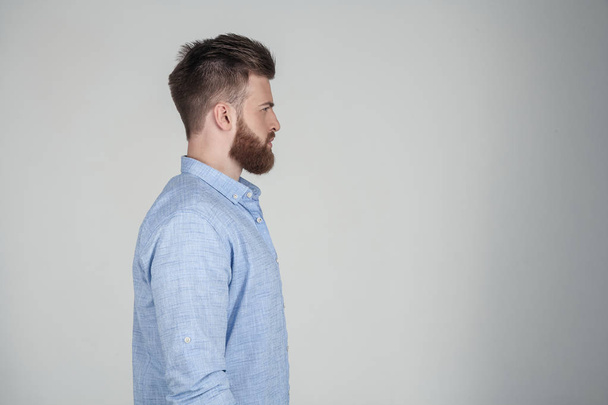 Красивий сексуальний бородатий чоловік, одягнений у повсякденний одяг він стоїть перед білим тлом у профілі
 - Фото, зображення