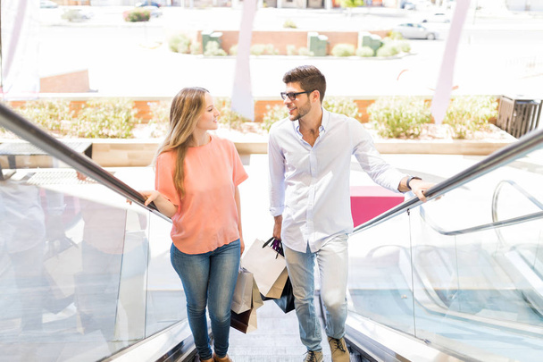 Caucasian man talking with girlfriend on escalator in shopping mall - Foto, afbeelding