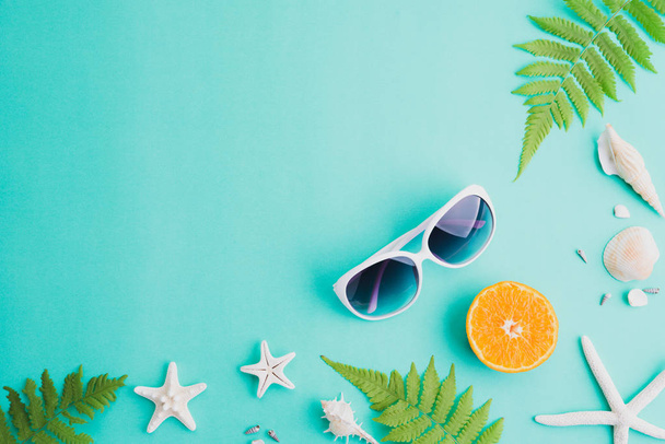 Аксессуары для пляжа солнцезащитные очки, морская звезда, апельсин, листья папоротника и морская раковина на зеленом фоне для летнего отдыха и отдыха
. - Фото, изображение