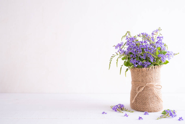 lovely purple flower in sack vase on white wooden table. - Фото, изображение