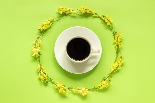 Cup of coffee and circular frame yellow wild flowers Linaria on green paper background Flat lay Top view Concept Good morning or Hello spring Template for postcard, text or your design - Фото, зображення