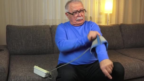 senior man wearing glasses in sweatshirt measures pressure - Filmati, video