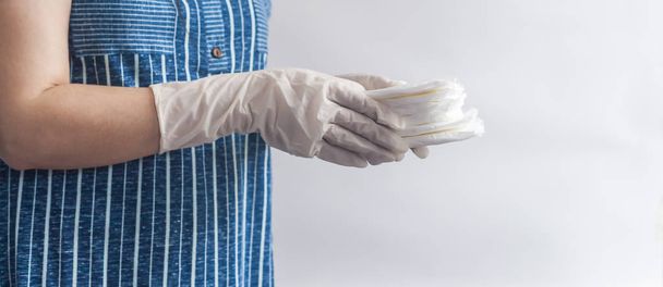 女性の衛生製品。白い背景に生理用ナプキンのスタックを保持する医療手袋の女性。女性の月経周期を示す期間日の概念. - 写真・画像