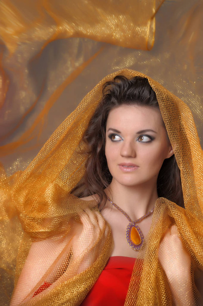 portrait of a beautiful brunette woman in a golden cape - Photo, image