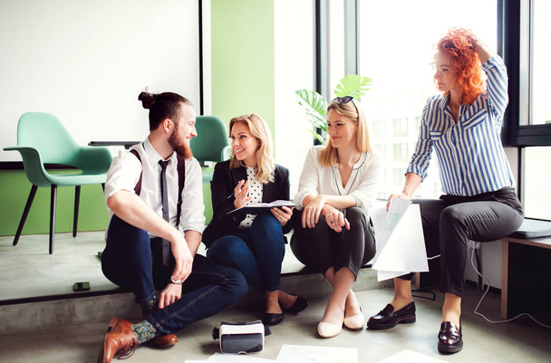 A group of young business people sitting on the floor in an office, talking. - Fotografie, Obrázek