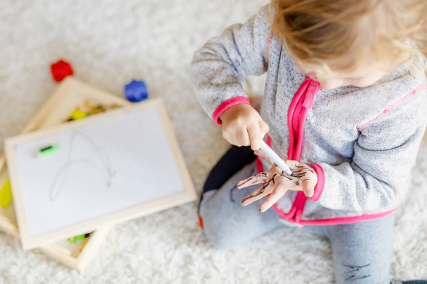 Nahaufnahme eines Kleinkindes, das mit Filzstiften Malerei lernt. Kleines Baby zeichnet auf Händen und Kleidern. - Foto, Bild