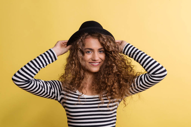 Portrait of a young woman with black hat in a studio on a yellow background. - Foto, Imagen