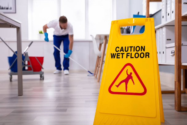 Male janitor with mop cleaning modern office floor - 写真・画像
