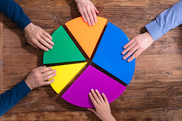 An Overhead View Of Businesspeople Connecting Pieces Of Multicolored Pie Chart On Wood Desk - Valokuva, kuva