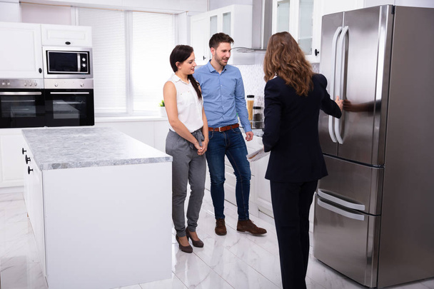 Agente inmobiliario profesional que muestra el refrigerador en casa a una pareja joven
 - Foto, imagen