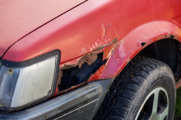 Rusty auto. Rode oude roestige auto. Fragment van een rode vleugel van een oude auto. Roestig gat in metaal - Foto, afbeelding