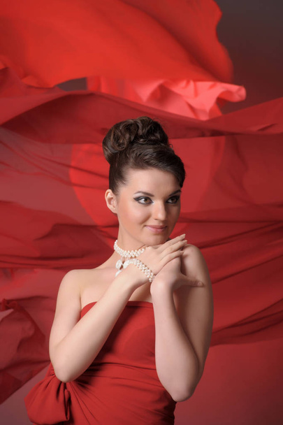 girl in a red dress  in the studio and flowing fabric - Foto, Imagem
