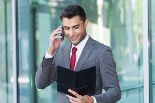 Businessman talking on the phone while reading his agenda - Foto, Bild