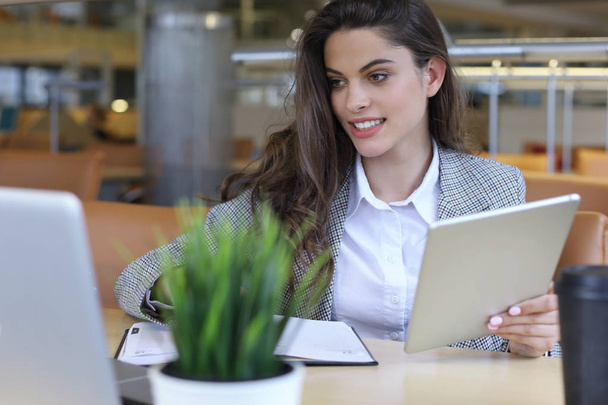 Young smiling businesswoman in office working on digital tablet. - Foto, afbeelding