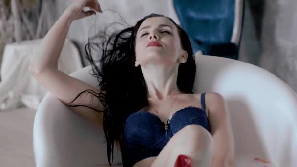 attractive black-haired girl in a blue bra enjoying in a bath with milk - Materiał filmowy, wideo