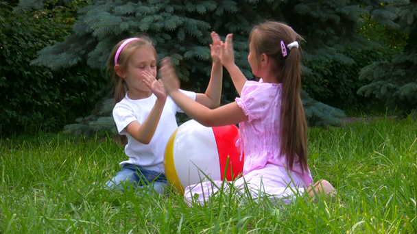 Девушки сидят с мячом на траве в парке и играют
 - Кадры, видео