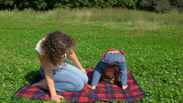 Girl looks upside down between legs and young woman in park - Video, Çekim