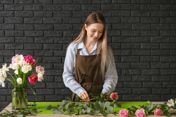 Floristin fertigt Blumenstrauß am Tisch vor dunklem Hintergrund - Foto, Bild