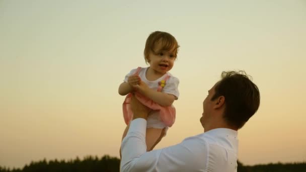 Isä leikkii tyttärensä kanssa puistossa. Isä heittää vauvansa taivaalle. onnellinen lapsuuden lapsi vanhempien kanssa. Isä heitti pojan pilveen. Onnellisen perheen käsite
. - Materiaali, video