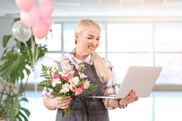 Florist with laptop and beautiful bouquet in shop - Фото, изображение